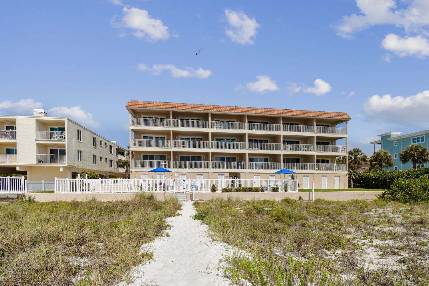 The Oceanside building seen from the beach, with a sand path leading up through the dunes
